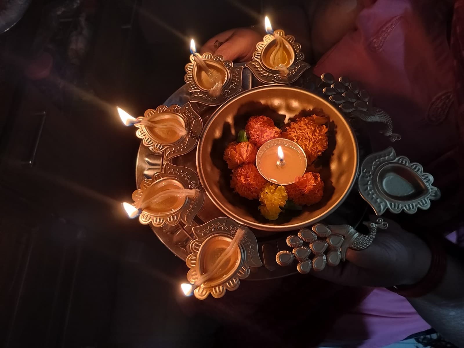 Lit oil lamps and flowers held on a brass plate during a traditional offering